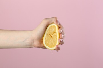 Woman squeezing lemon on pink background, closeup