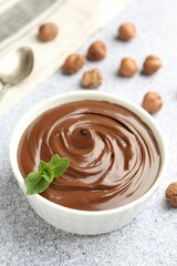 Tasty chocolate spread with mint in bowl and hazelnuts on grey textured table