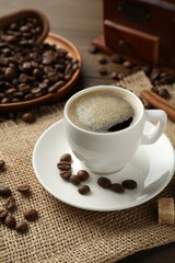 Aromatic coffee in cup, beans, brown sugar and cinnamon on table, closeup