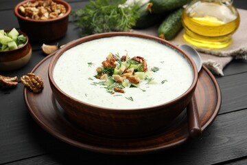 Tasty cucumber soup with dill and walnuts served on black wooden table, closeup