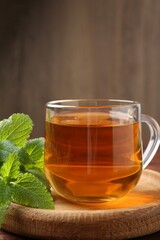 Aromatic lemon balm tea in glass cup and fresh leaves on wooden table