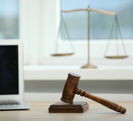 Laptop, judge's gavel and scales on wooden table in office