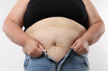 Overweight woman trying to put on tight jeans against white background, closeup