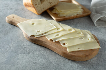 A view of several thin slices of American style Swiss cheese, on a wood cheese board.