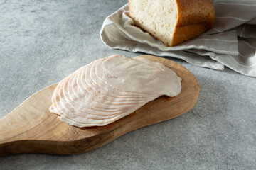 A view of a stack of turkey breast slices, on a wooden cheese board.