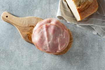 A top down view of a pile of uncured ham deli slices, on a wood cheese board.