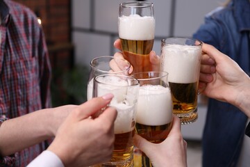 Friends clinking glasses of beer indoors, closeup