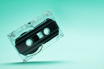 One audio cassette in air on turquoise background, closeup. Space for text
