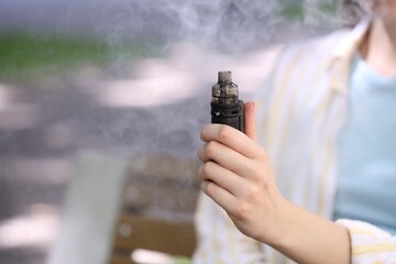 Young woman with electronic smoking device outdoors, closeup. Space for text