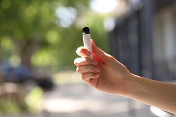 Young woman with electronic smoking device outdoors, closeup. Space for text