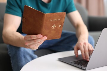 Man with passport using laptop at table indoors, closeup