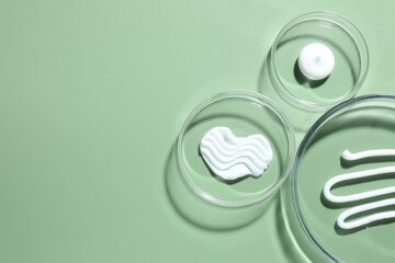 Different cosmetic products in Petri dishes on green background, flat lay. Space for text