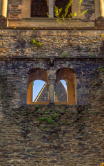 Close-up of a Romanesque stone window with arches and a column, and plant branches on the stone wall illuminated by evening light at the Abbey of Sainte-Foy, Conques.