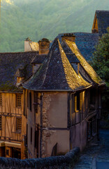 Tiled roofs of medieval houses beautifully illuminated by the golden light of sunset in a picturesque corner of the medieval French village of Conques, France.