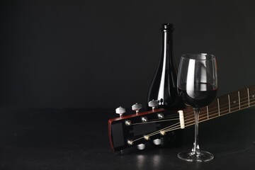 Acoustic guitar and red wine on black table, closeup. Space for text