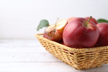 Spoiled apple and good ones in basket on white wooden table, closeup. Space for text
