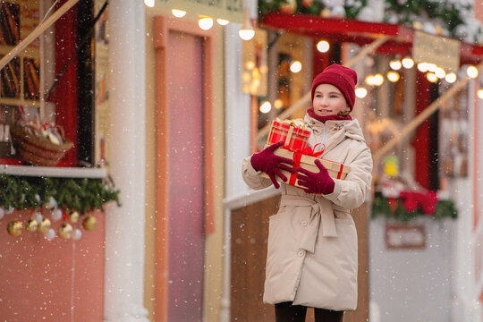 girl carrying gifts walks along shopping arcade of Christmas market.