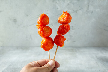 A view of a hand holding some skewers of deep fried kwek kwek.