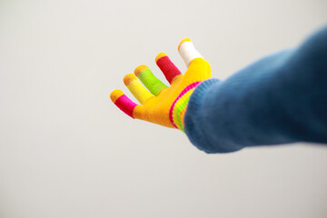 A vibrant hand, covered in a colorful glove with rainbow accents and painted fingertips against a stark white backdrop