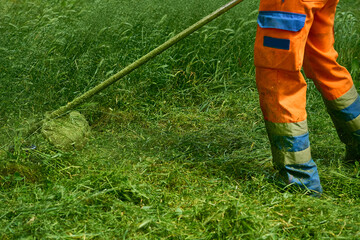 A park worker in an orange jumpsuit mows the grass with a motorized mower