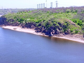 View from the Arch Bridge on the calm water surface of the Dnieper that washes the sandy shores and rocky cliffs of Khortytsia Island.