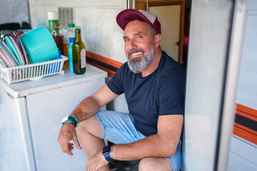 Cheerful camper relaxing on caravan doorstep, savoring tranquil summer moment amid scenic outdoor environment