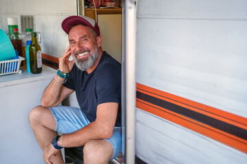 Bearded traveler relaxing on camper van doorstep, enjoying freedom of nomadic lifestyle with scenic background