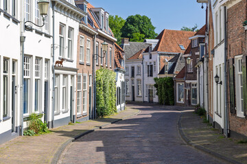 A picturesque, winding cobblestone street in Amersfoort, flanked by traditional Dutch houses with varying facades and a clear blue sky above.