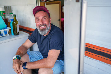 Portrait of a smiling camper sitting on the doorstep of his caravan, enjoying the outdoor lifestyle