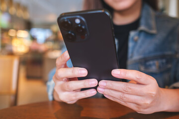 Closeup image of a woman holding and using mobile phone in cafe