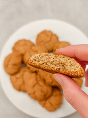 Hand holding half of a molasses oat cookie above plate of cookies
