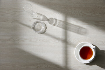 A glass and tea on a wooden table with natural light streaming in through a window.