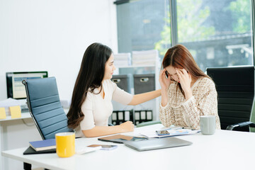 Asian woman comforts her distressed coworker in office. Concept of workplace stress, burnout,...