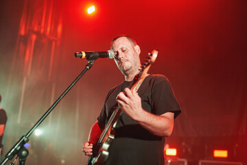 Male musician singing and playing electric guitar on stage under red lights