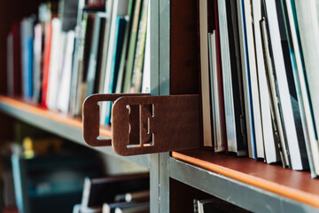 Books on library shelves with visible section markers. Some volumes on a table in front of blurred...