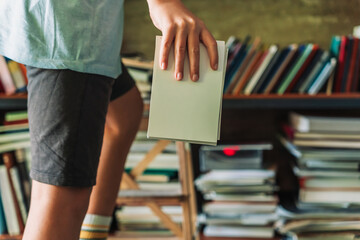 Boy placing a book on a high shelf using a small stool in a library setting. Learning and...