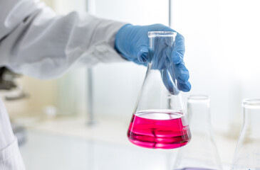 The scientist wear blue nitrile gloves holding Erlenmeyer Conical flask, with purple violet solvent...