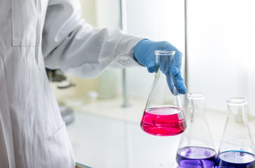 Scientist in a laboratory holding a volumetric flask containing a purple chemical. Titration...