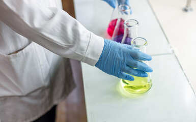 The scientist wear blue nitrile gloves holding Erlenmeyer Conical flask, with purple violet solvent...