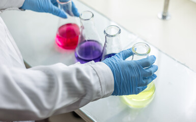The scientist wear blue nitrile gloves holding Erlenmeyer Conical flask, with purple violet solvent...