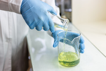 Scientist or medical in lab coat holding test tube with reagent, mixing reagents in glass flask in...