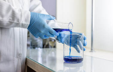 Scientist or medical in lab coat holding test tube with reagent, mixing reagents in glass flask in...