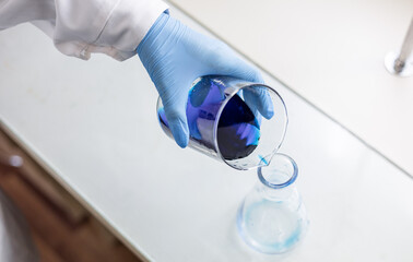 Scientist or medical in lab coat holding test tube with reagent, mixing reagents in glass flask in...
