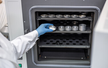 A female laboratory assistant chemist places a container with the substance being studied into a...