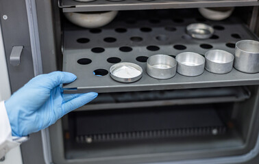 A female laboratory assistant chemist places a container with the substance being studied into a...