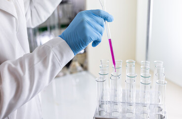 Scientist dripping color liquid into test tube in laboratory. Pipette with a drop and scientific...