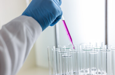 Scientist dripping color liquid into test tube in laboratory. Pipette with a drop and scientific...