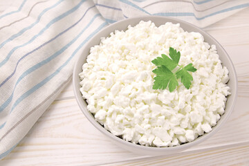 Farm cheese in a bowl on a light wooden background. Cottage cheese with parsley.