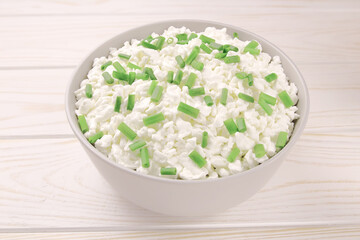 Farm cheese in a bowl on a light wooden background. Cottage cheese with young green chives.