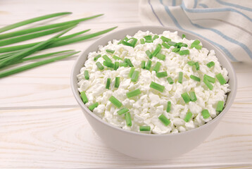 Farm cheese in a bowl on a light wooden background. Cottage cheese with young green chives.